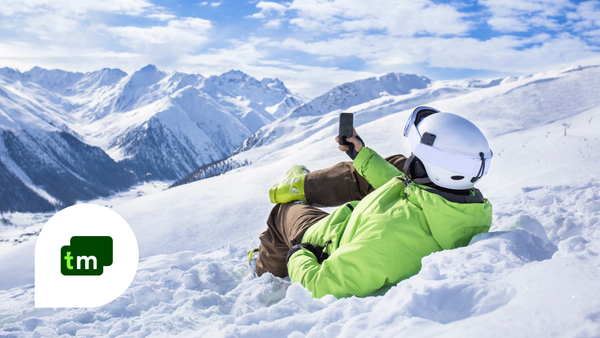 Et menneske ligger i snøen og holder en telefon foran seg