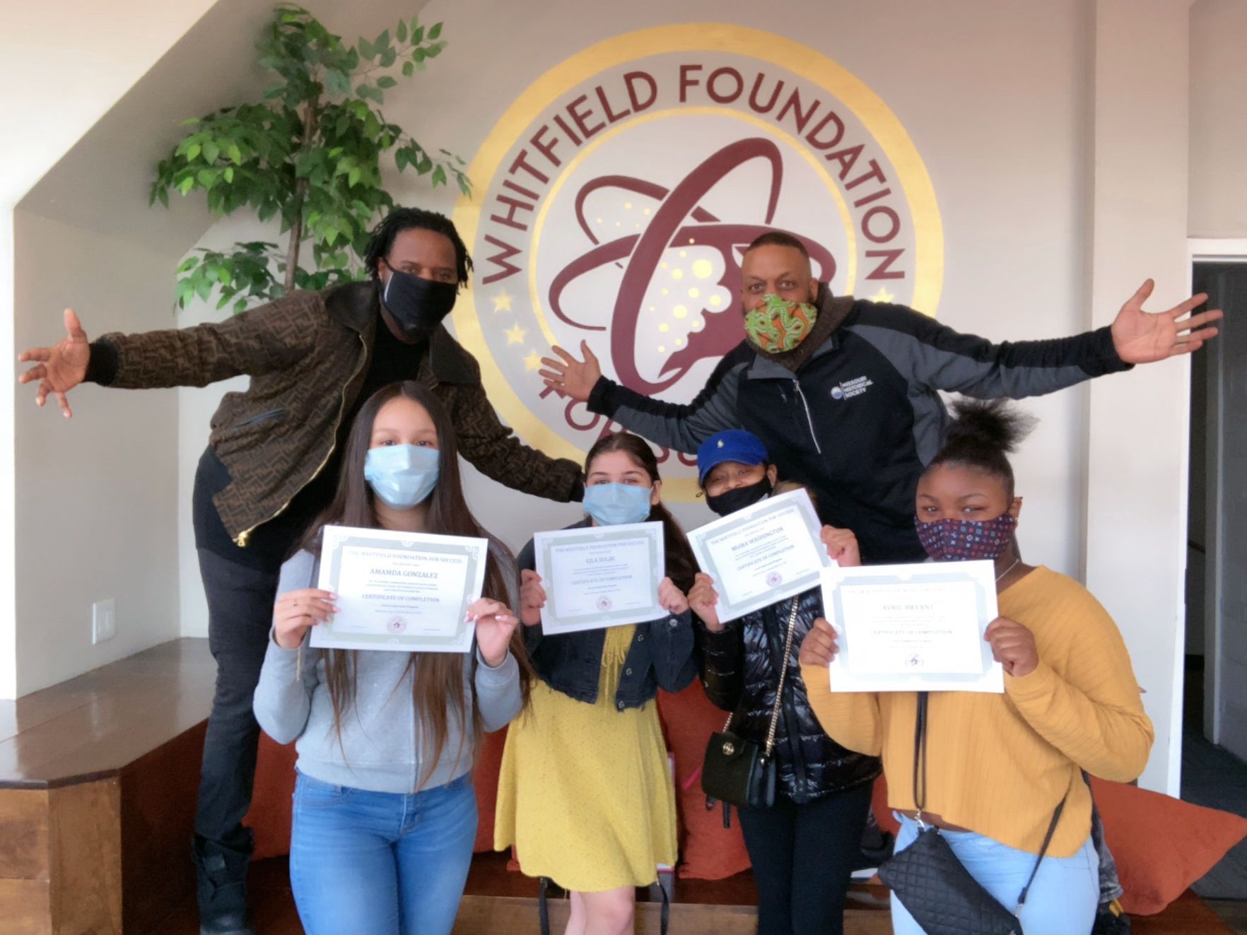 Program participants holding certificates in front of the Whitfield Foundation wall logo