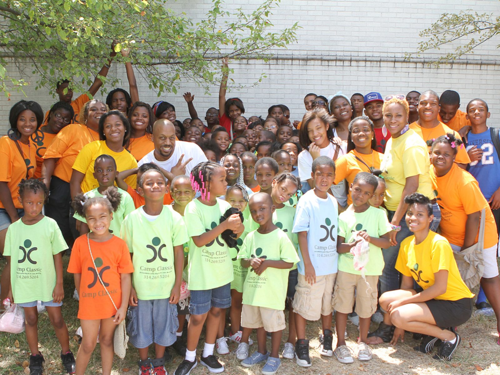 Children and adults posing together outdoors in matching yellow shirts