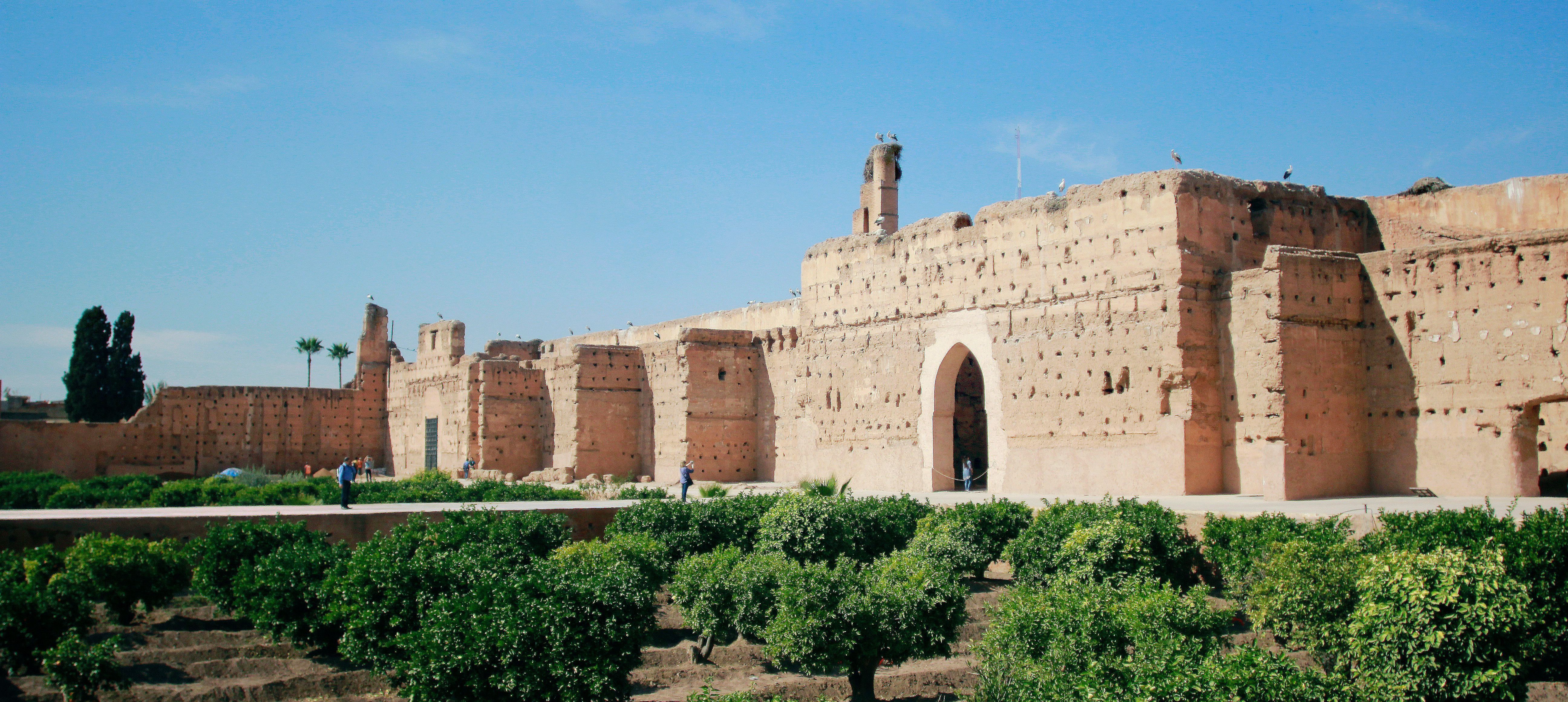 Tall, eroded rammed-earth walls of the El Badi Palace above orange-tree gardens