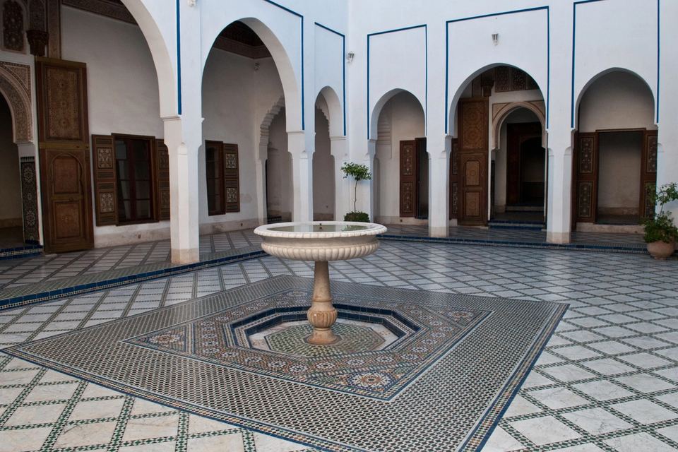 Zellige-tiled courtyard with a central fountain, surrounded by galleries of white columns