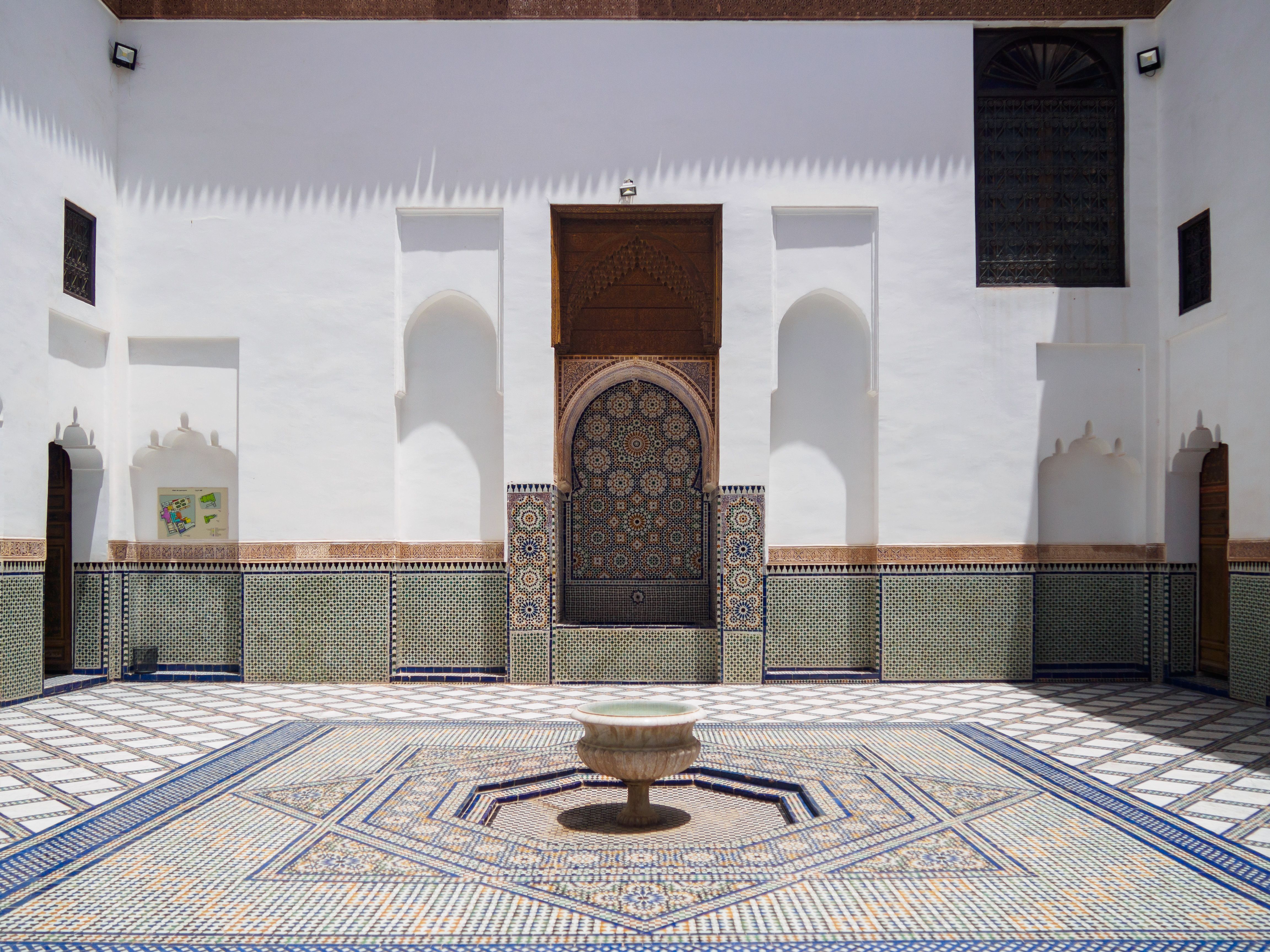 White patio with a central fountain and zellige floor, surrounded by carved wooden doors