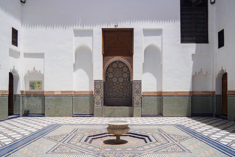 White patio with a central fountain and zellige floor, surrounded by carved wooden doors