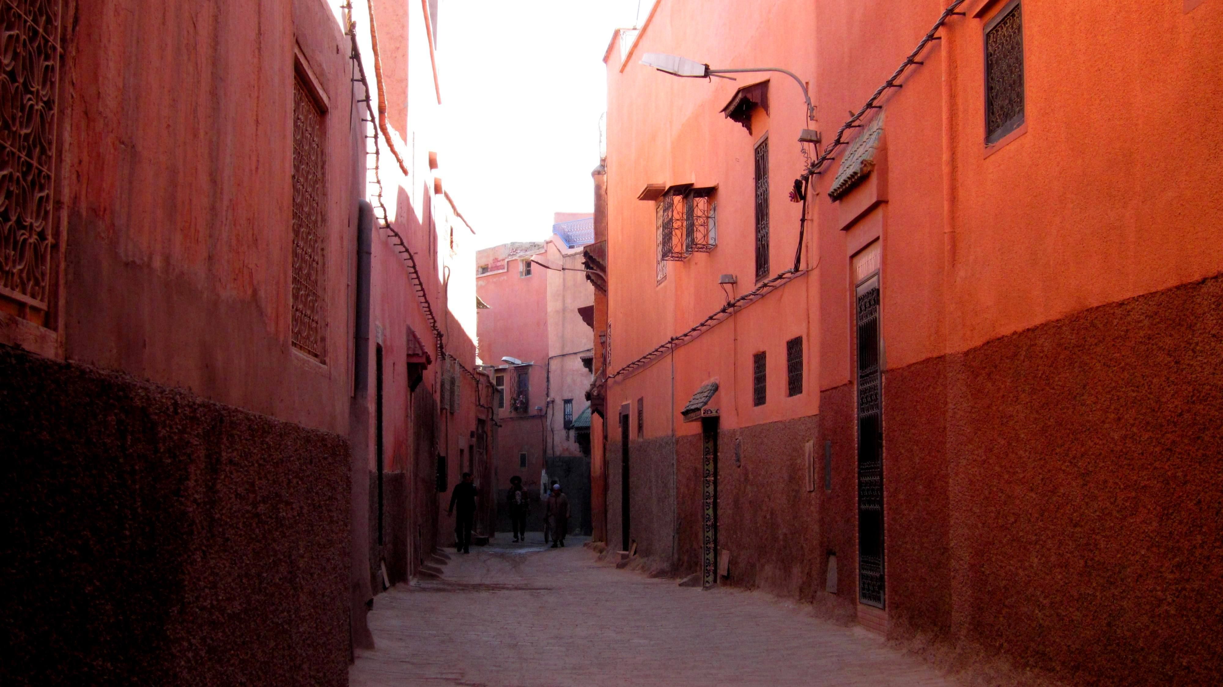 Narrow derb in the Marrakech medina between high ochre and red walls, in raking light