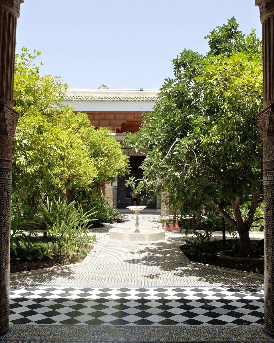 Jardin intérieur planté d'orangers vu entre deux colonnes, sol en damier de zellige