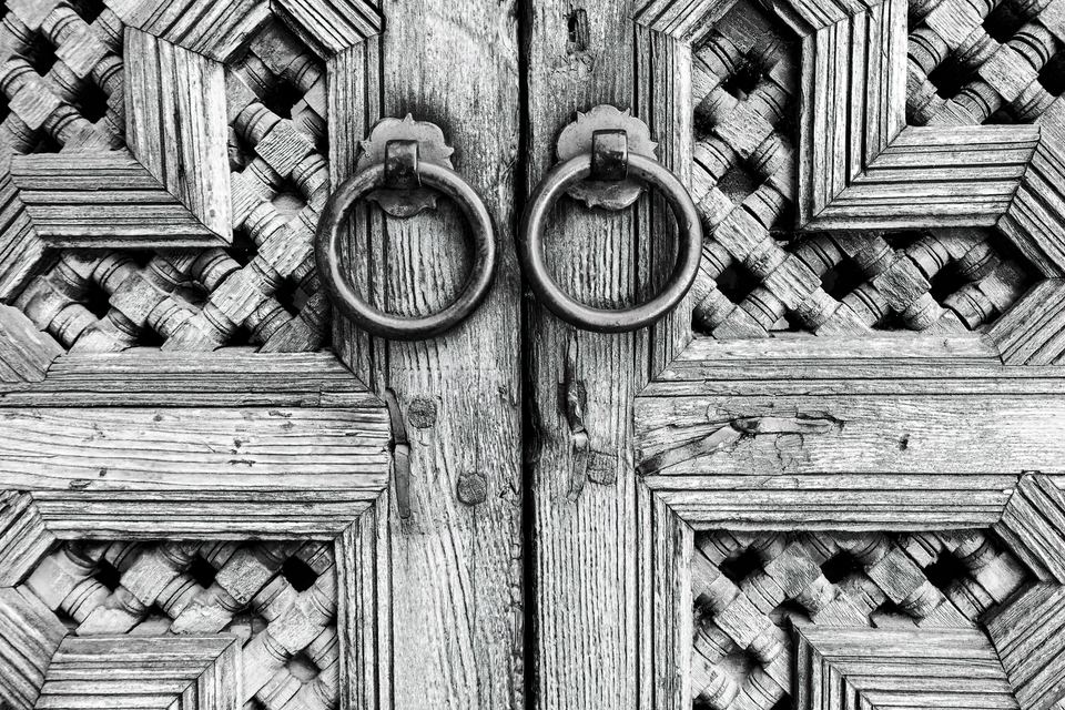 Carved wooden door leaves with geometric patterns and ring knockers, in black and white