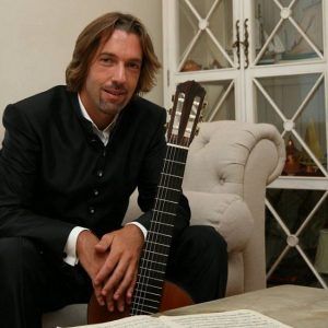 Adriano Del Sal sitting on a couch with his guitar.