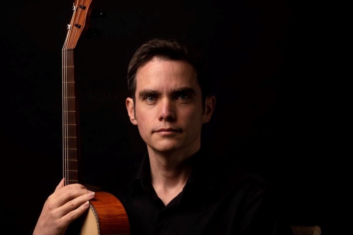 Oman Kaminsky holding a guitar while looking at the reader