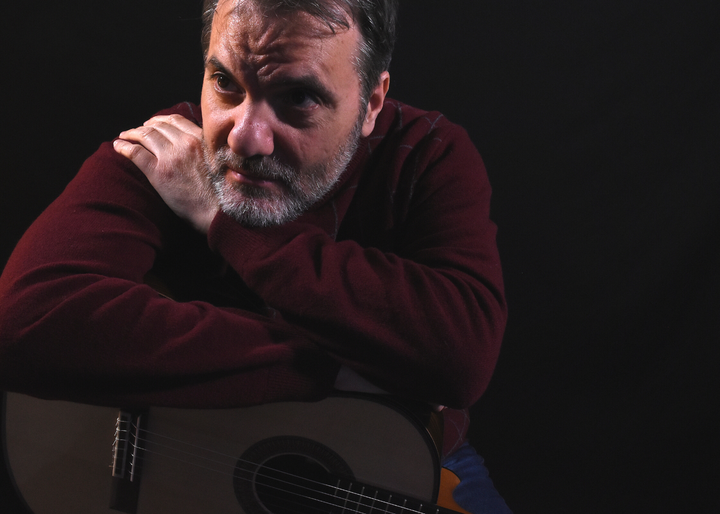 Carlo Marchione in a dark room leaning over his guitar.