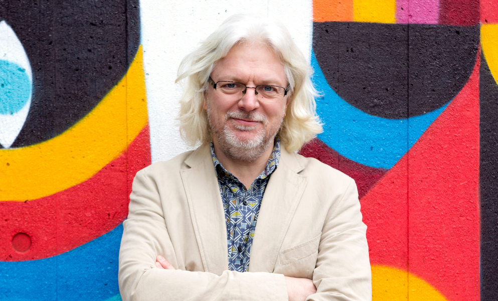Stephen Goss looking at the reader in front of a very colourful background