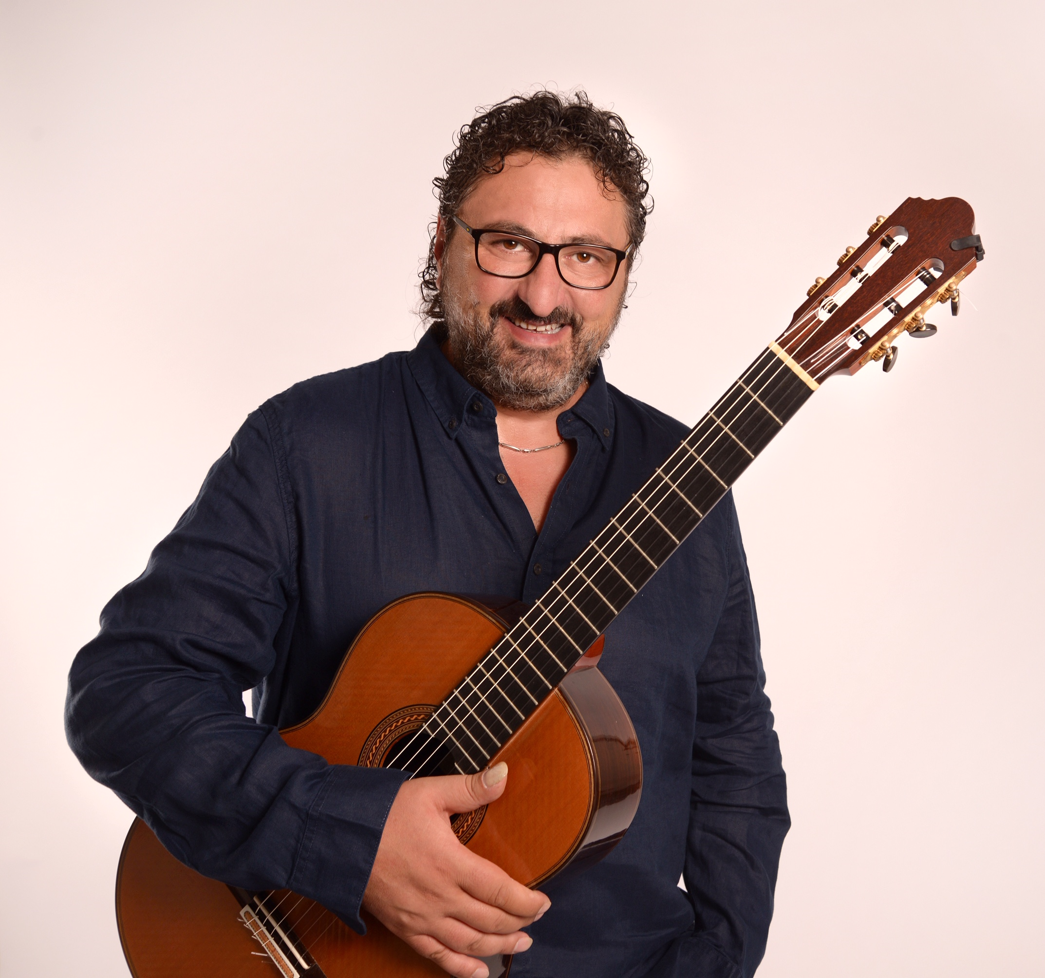 Aniello sitting with his guitar with a big smile on his face.