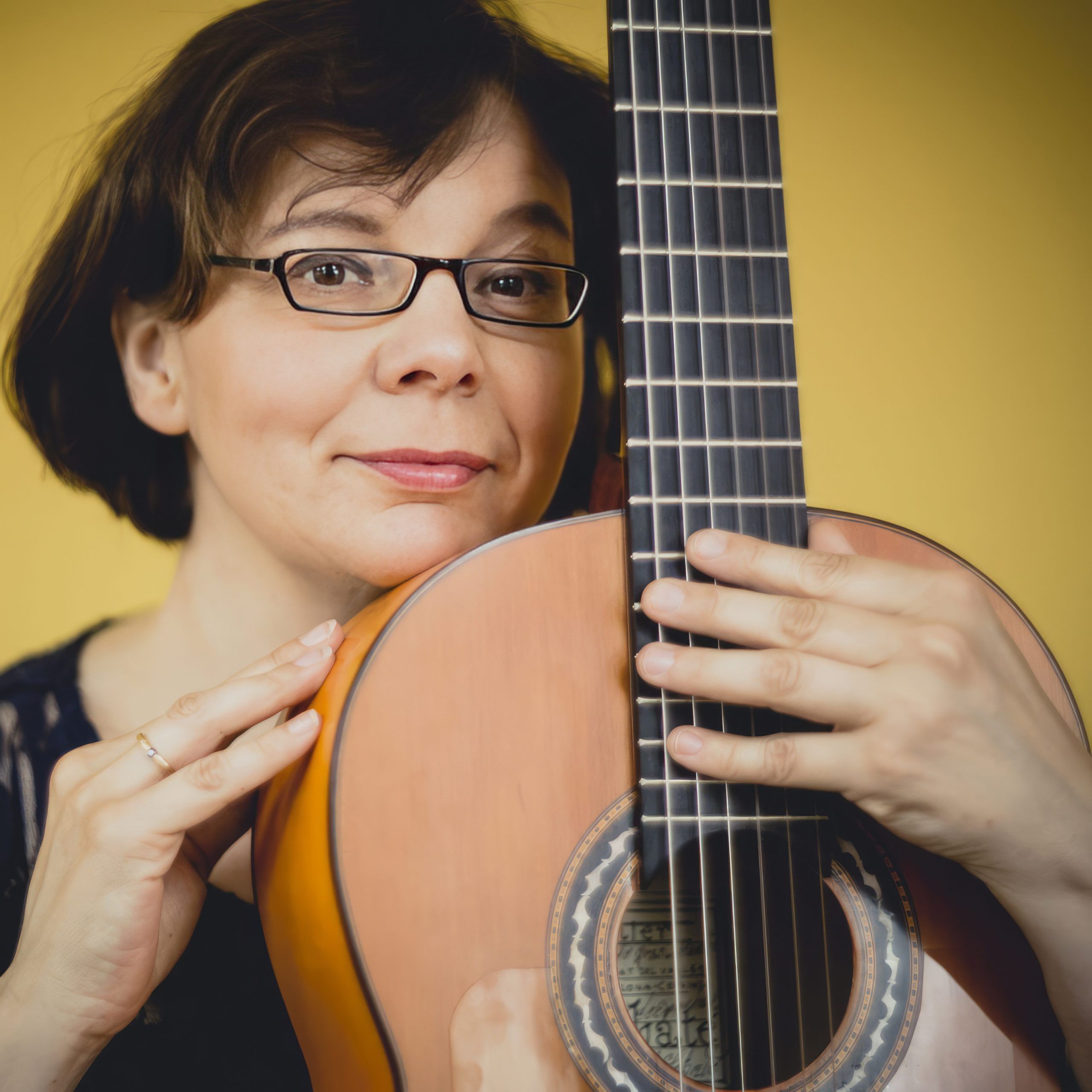 Eva Sabate Costa holding a guitar in front of here while looking inquisitively at the viewer