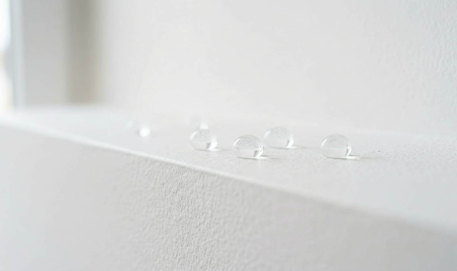 Effetto idrorepellente nanotecnologico su intonaco bianco: gocce d'acqua che non penetrano nel muro grazie alla barriera invisibile di Ector RP-50.