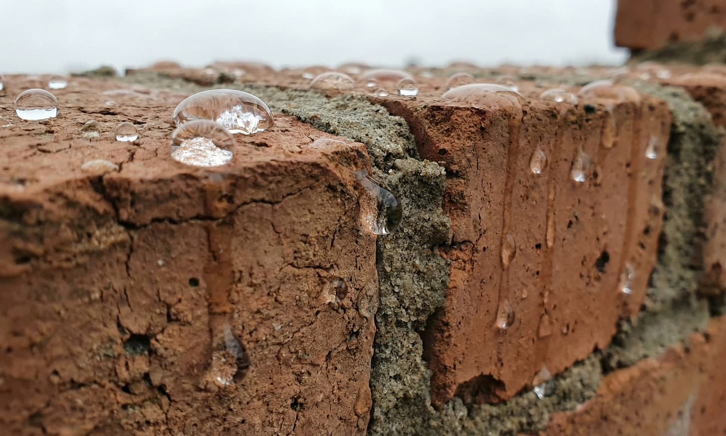 Dettaglio macro di un muro in mattoni antichi trattato con ECTOR RP-50: le gocce di pioggia rimangono in superficie come sfere senza penetrare nel materiale poroso.