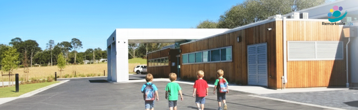 Four young children walking towards the entrance of the modern Remarkable Kids daycare building on a sunny day.