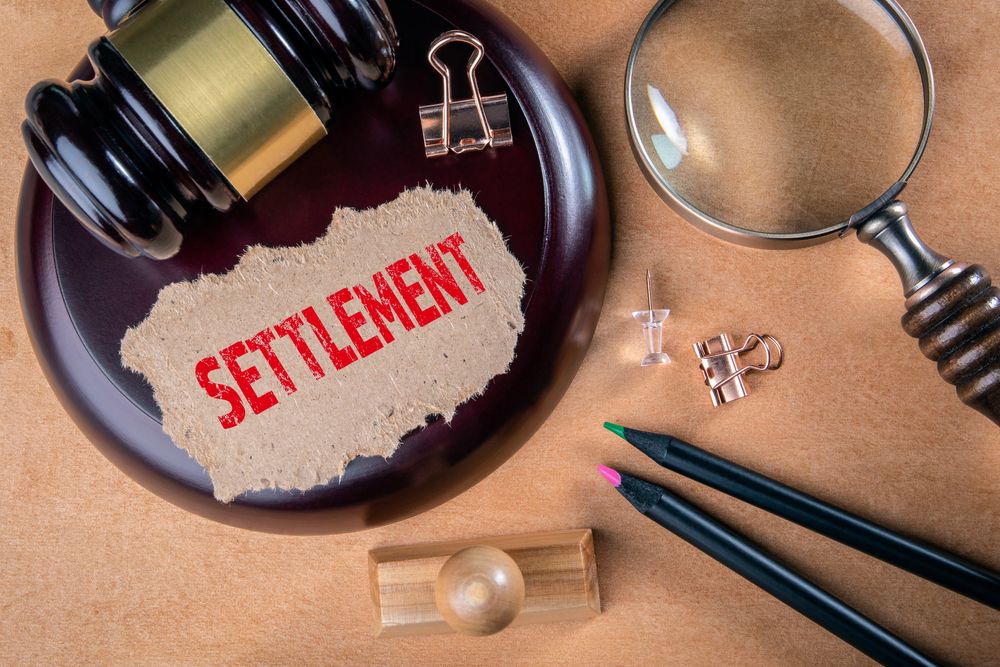 Gavel and magnifying glass beside paper labeled “settlement,” representing an early settlement offer after a birth injury claim.
