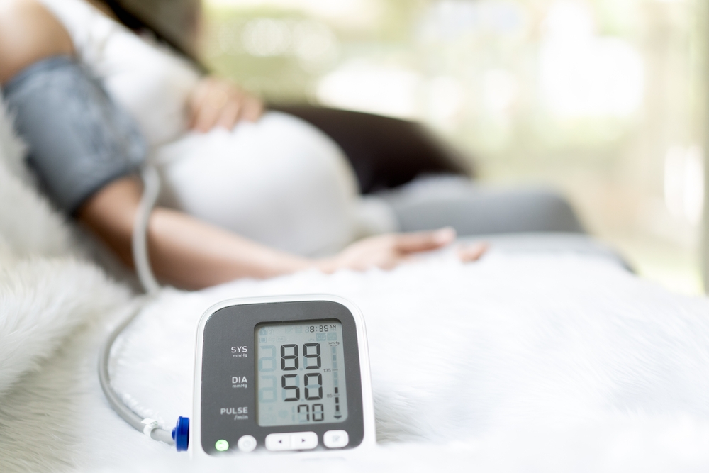 Image A pregnant woman monitoring their blood pressure at home with a digital monitor, illustrating how to identify a potential failure to diagnose preeclampsia.