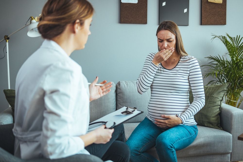 Pregnant woman meeting with a doctor during flu season to discuss fever, respiratory symptoms, and pregnancy safety in a prenatal care visit.