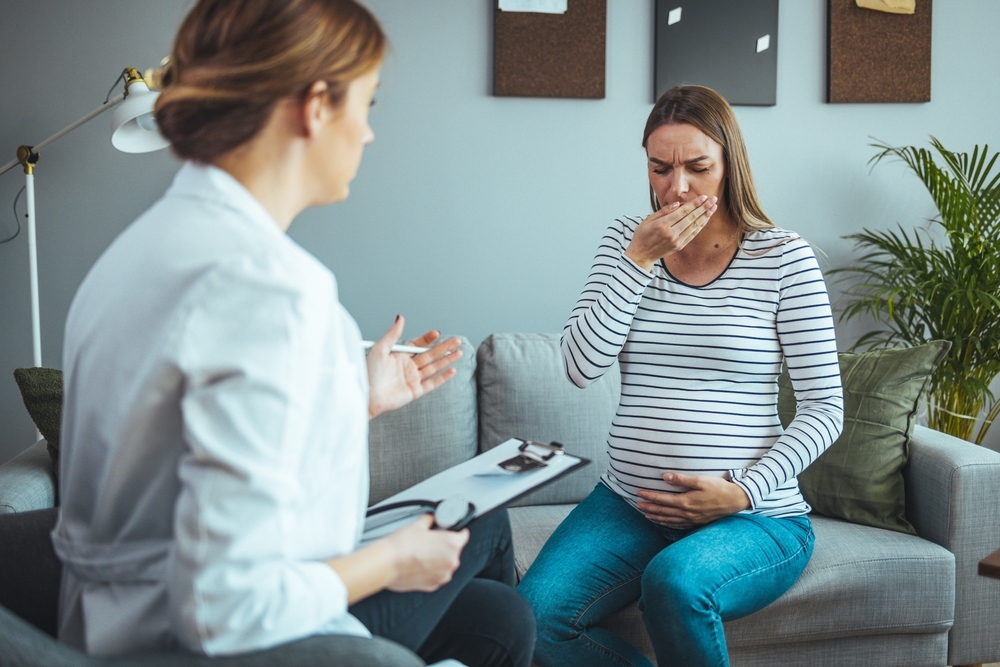 Image Pregnant woman meeting with a doctor during flu season to discuss fever, respiratory symptoms, and pregnancy safety in a prenatal care visit.