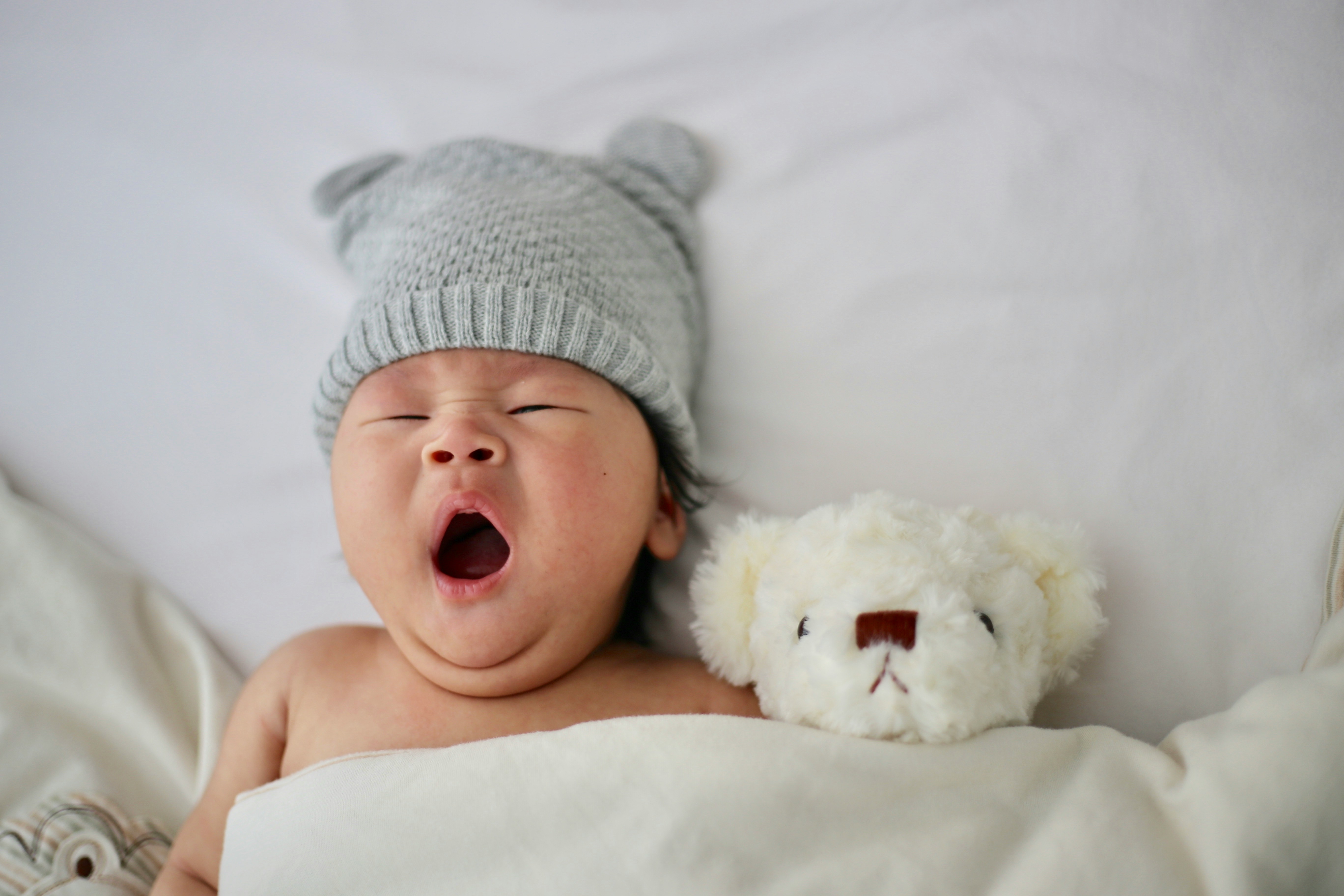 Image Yawning newborn in a knit hat lying beside a teddy bear, representing babies with rare chromosome disorders or birth injuries.