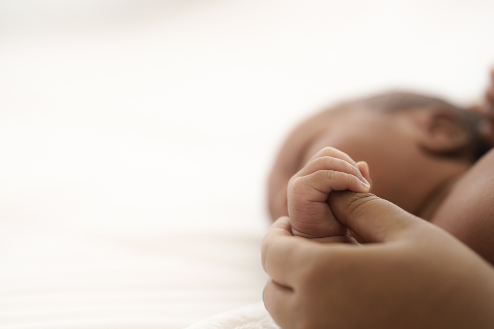 Image Close-up of a newborn baby’s hand holding an adult’s finger, representing the vulnerability of infants and the care required in neonatal medicine.