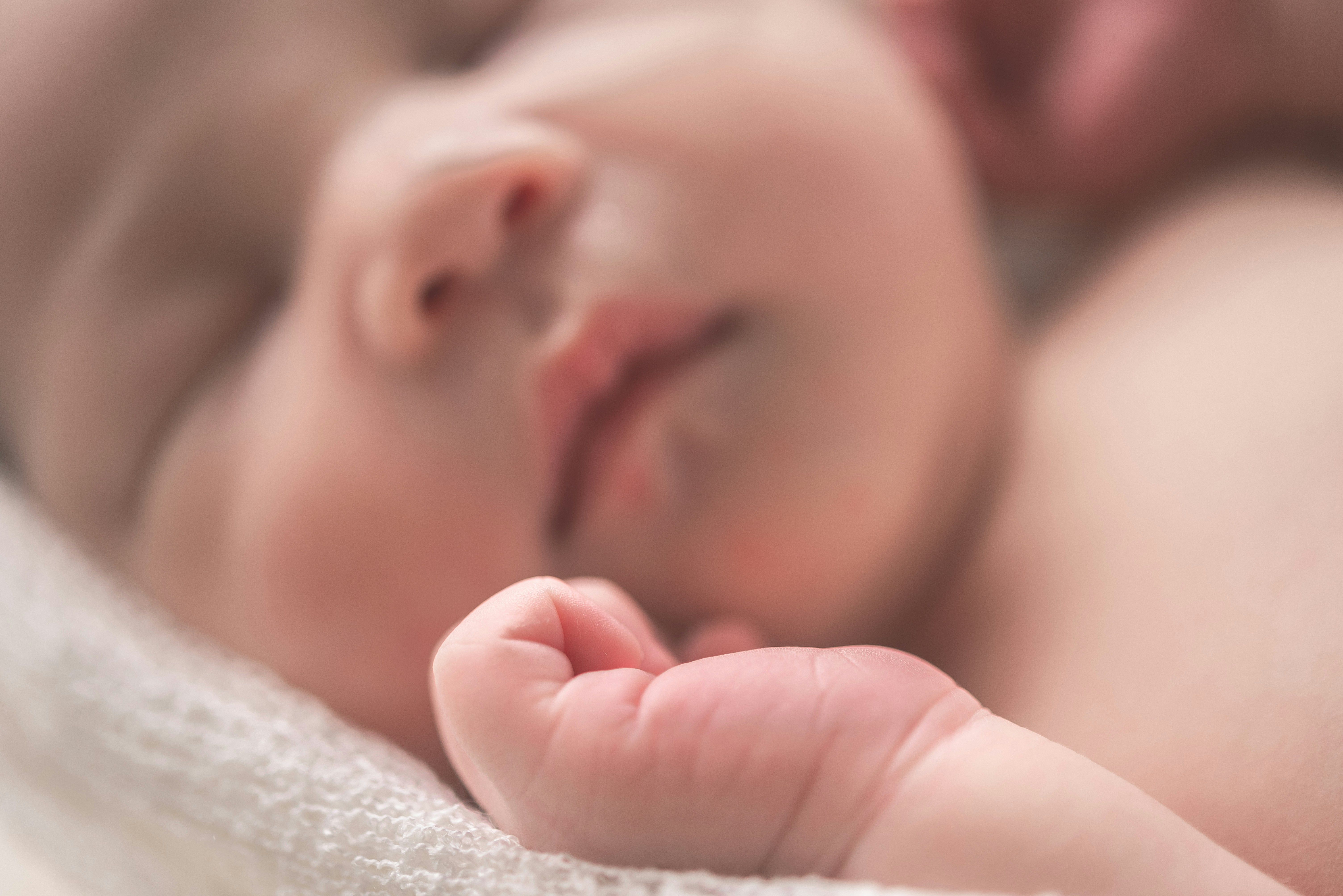 Sleeping newborn baby with tiny hand curled in the foreground, representing infants affected by congenital CMV.