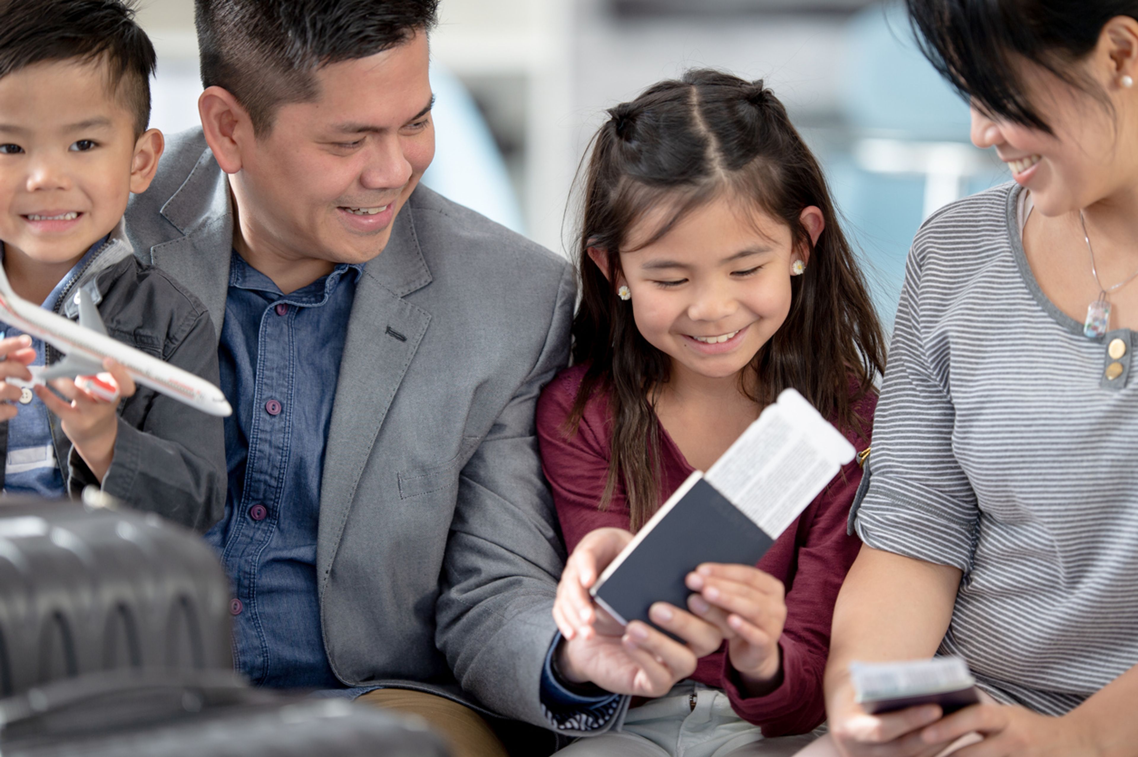 A young family sits together on an airport bench holding their passports and travel documents.