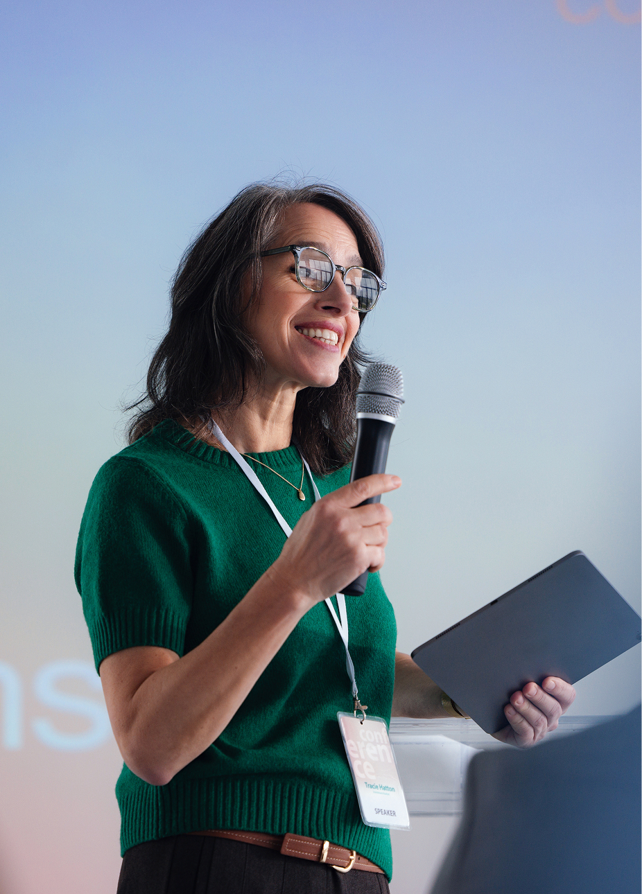 A professor speaking at a conference with a microphone and tablet