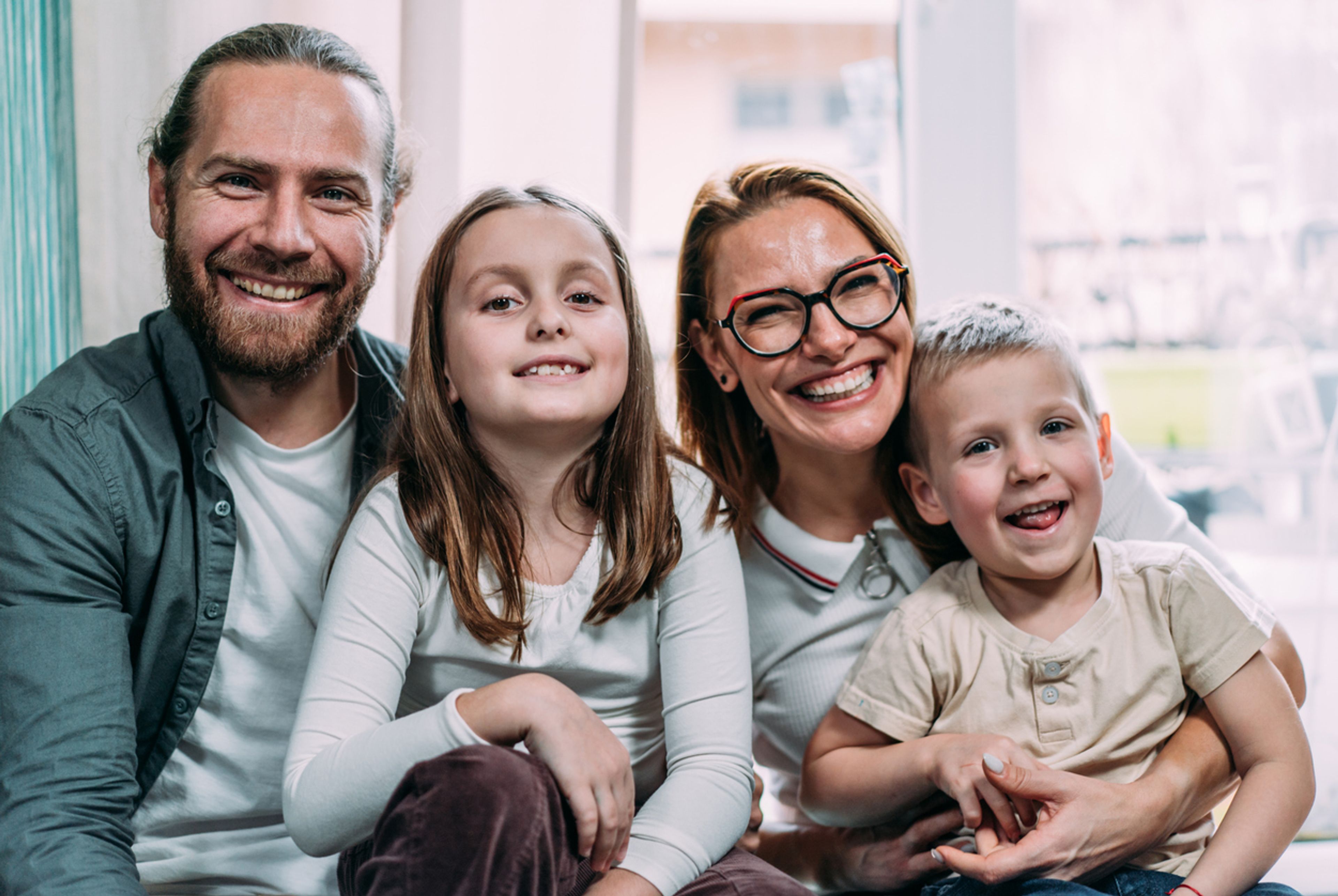 Portrait of cheerful parents with their two kids sitting on the sofa in living room at home.