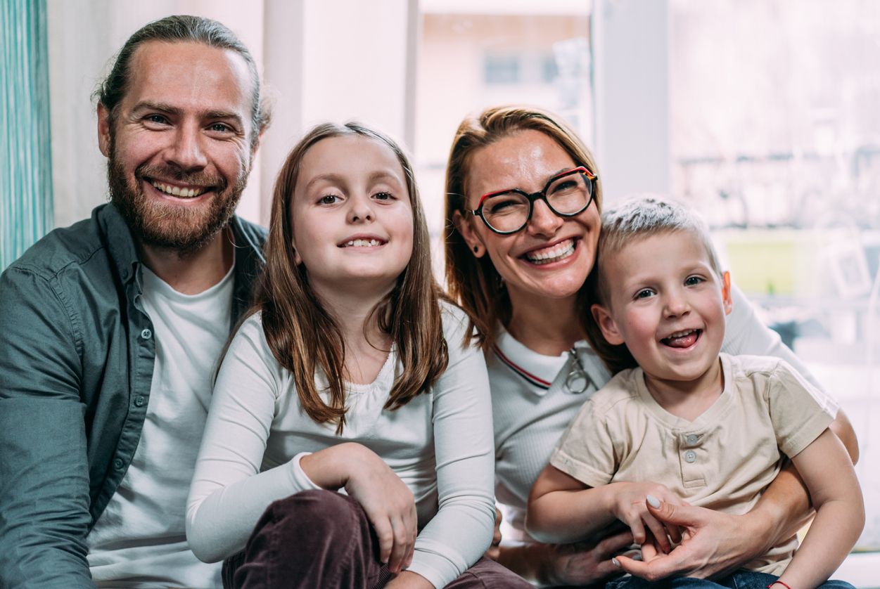 Portrait of cheerful parents with their two kids sitting on the sofa in living room at home.