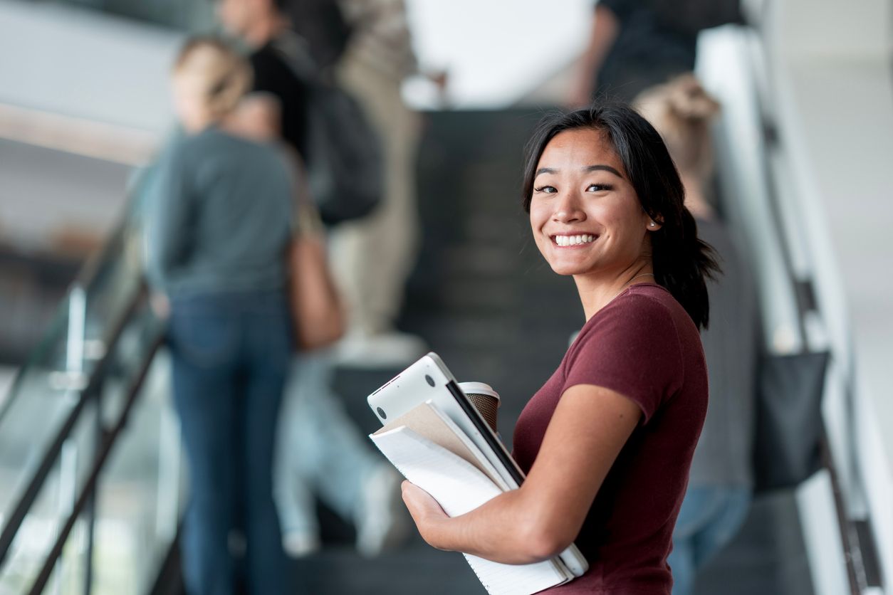 College student smiling and holding her notebooks and laptop.