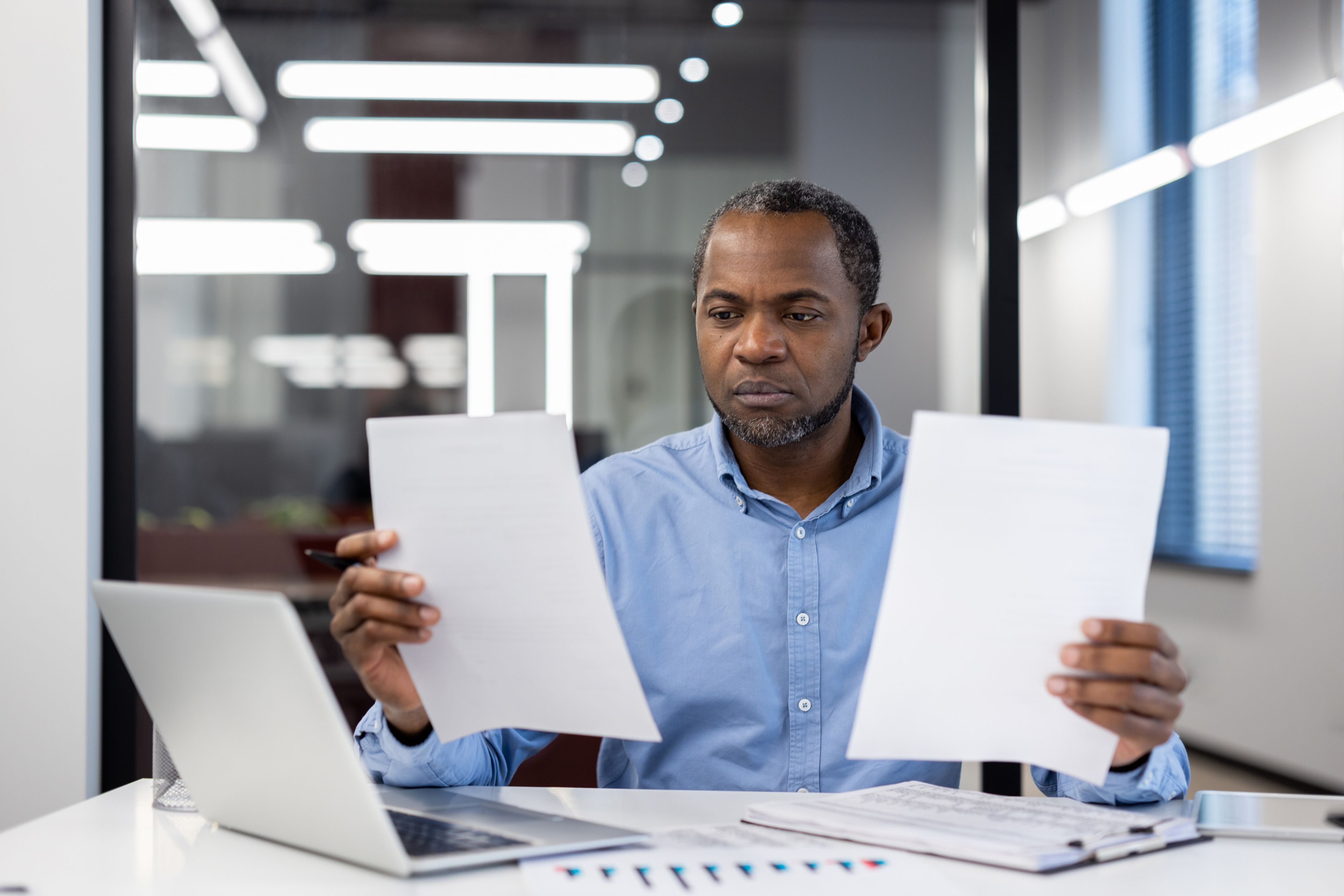 A man sitting at a desk is holding up two documents as he considers his visa options.