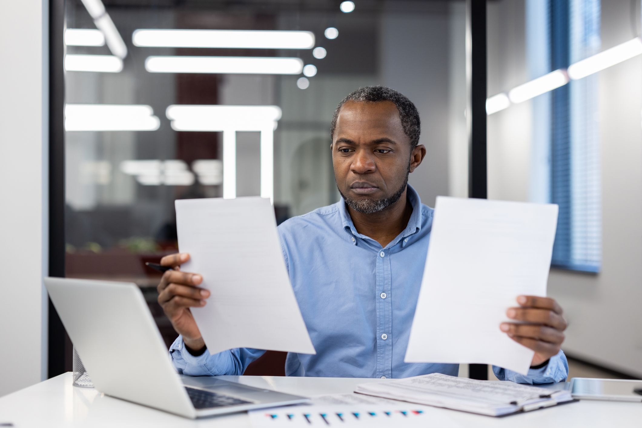 A man sitting at a desk is holding up two documents as he considers his visa options.