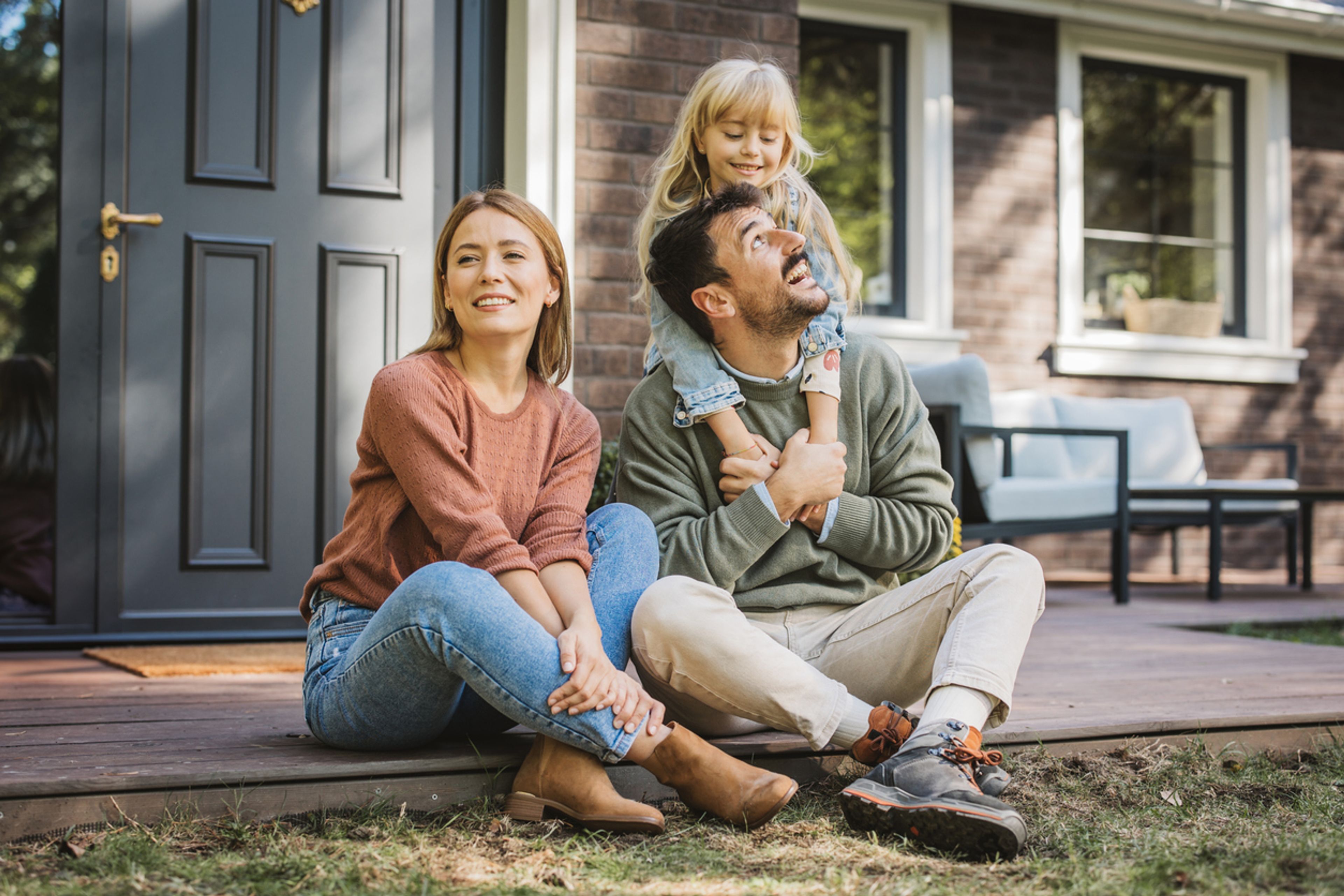 Family with young child sitting in front of their house.