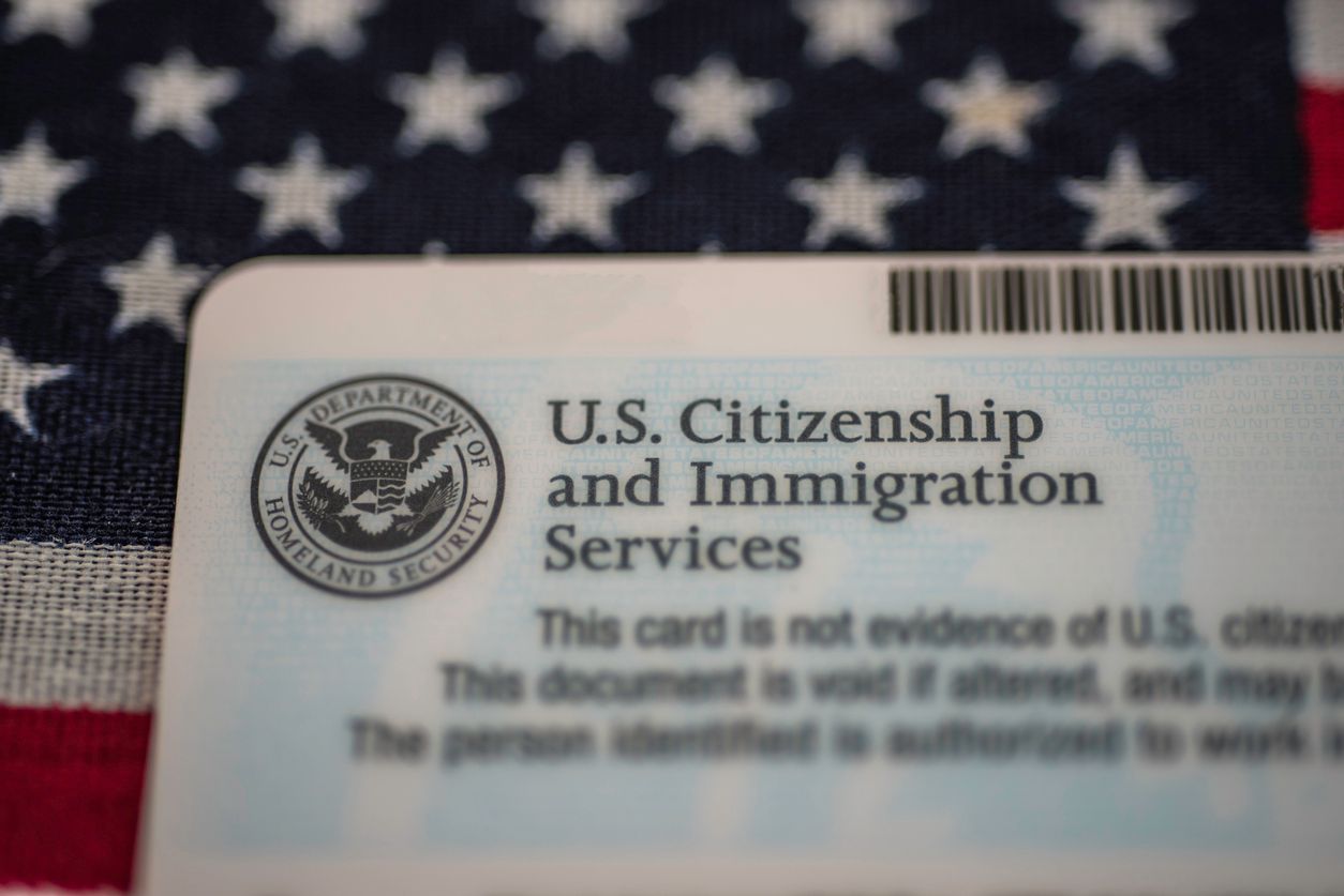 USCIS green card on a U.S. flag, illustrating TPS work authorization and SAVE verification updates.