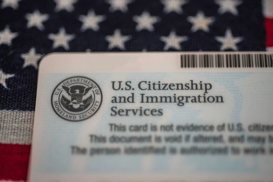 USCIS green card on a U.S. flag, illustrating TPS work authorization and SAVE verification updates.