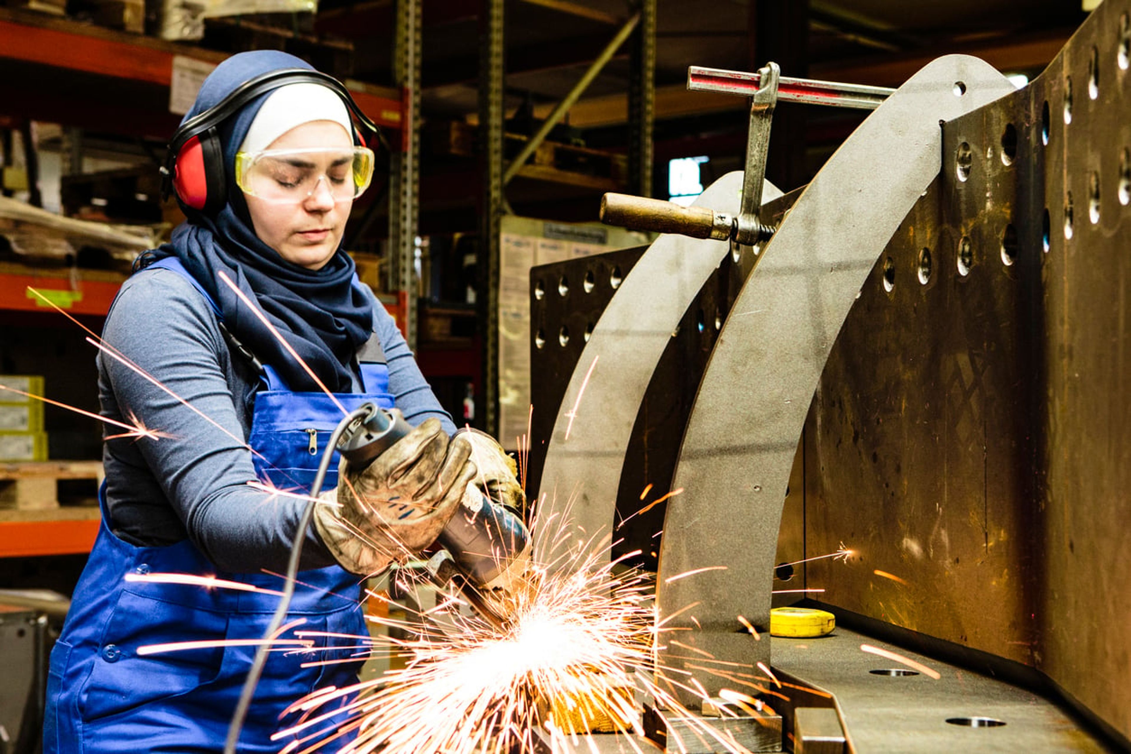 Worker welds steel with a grinder in her workshop.