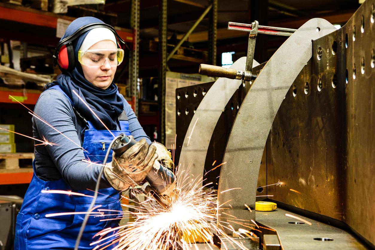 Worker welds steel with a grinder in her workshop.