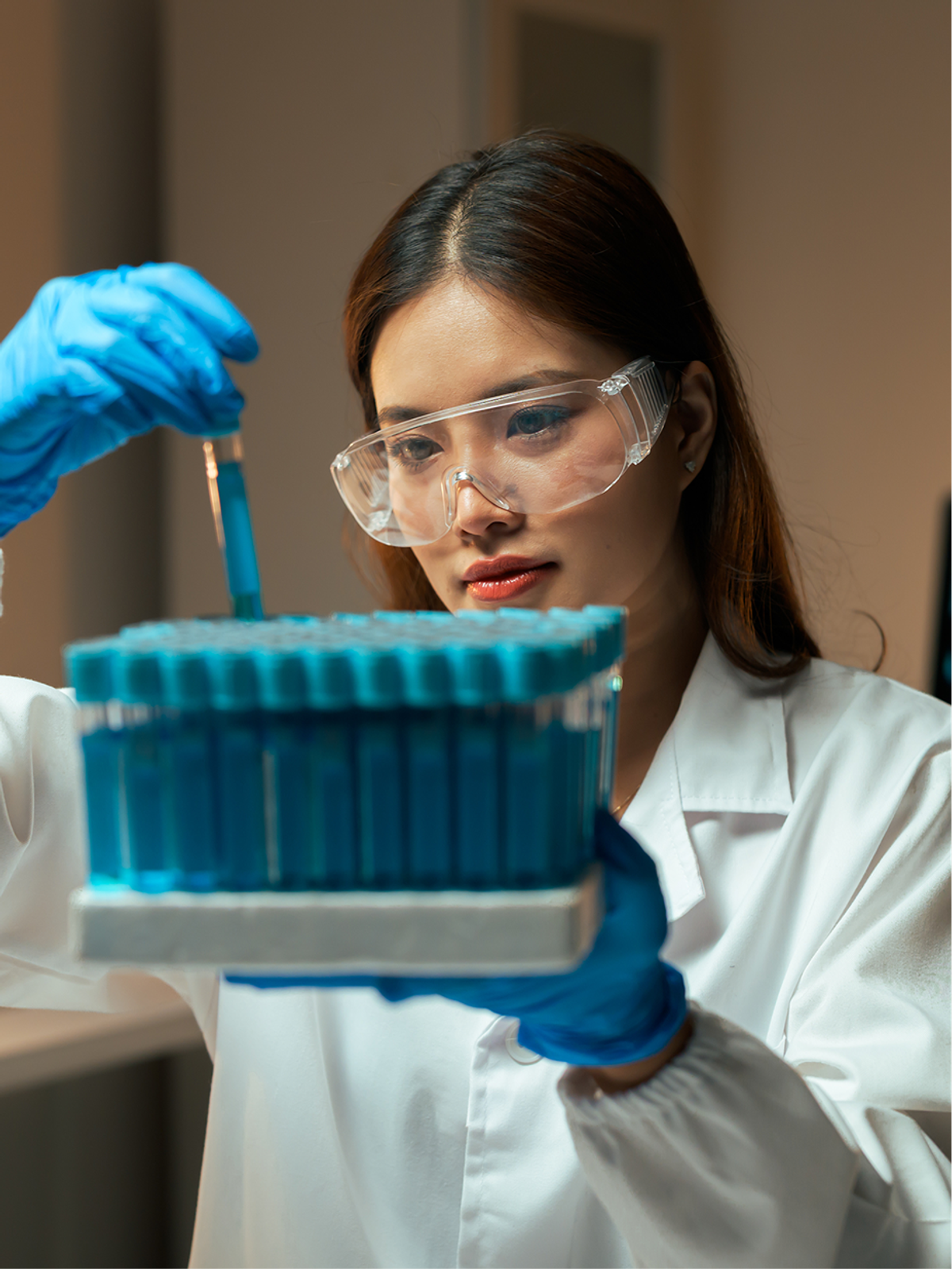 A researcher in a lab coat handling blue test tubes