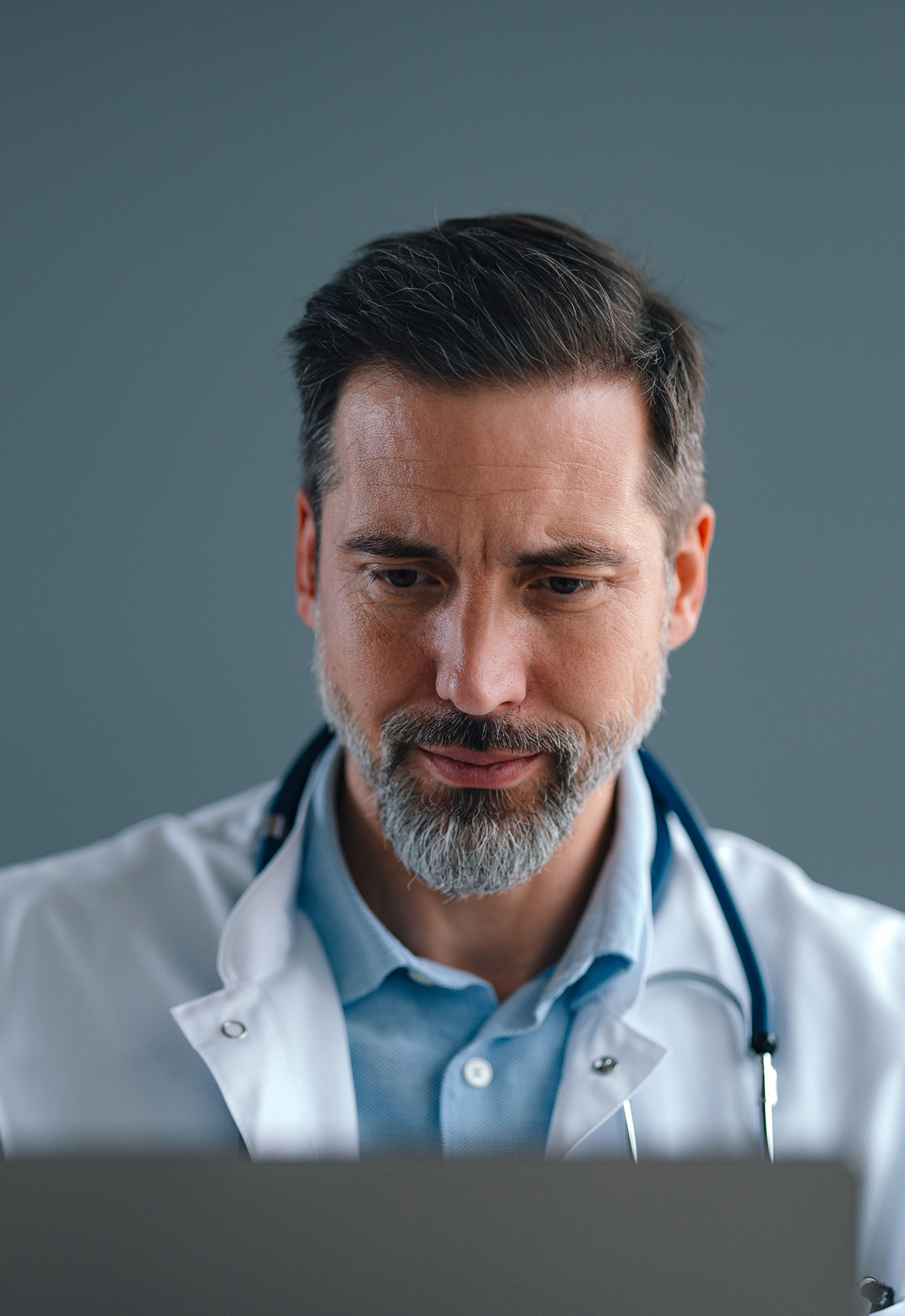 A physician in a lab coat reviewing work on a laptop