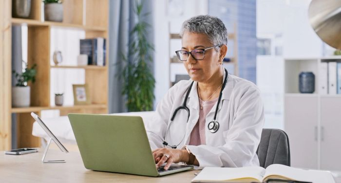 An older woman doctor sits at a laptop, typing an EB-2 NIW recommendation letter.