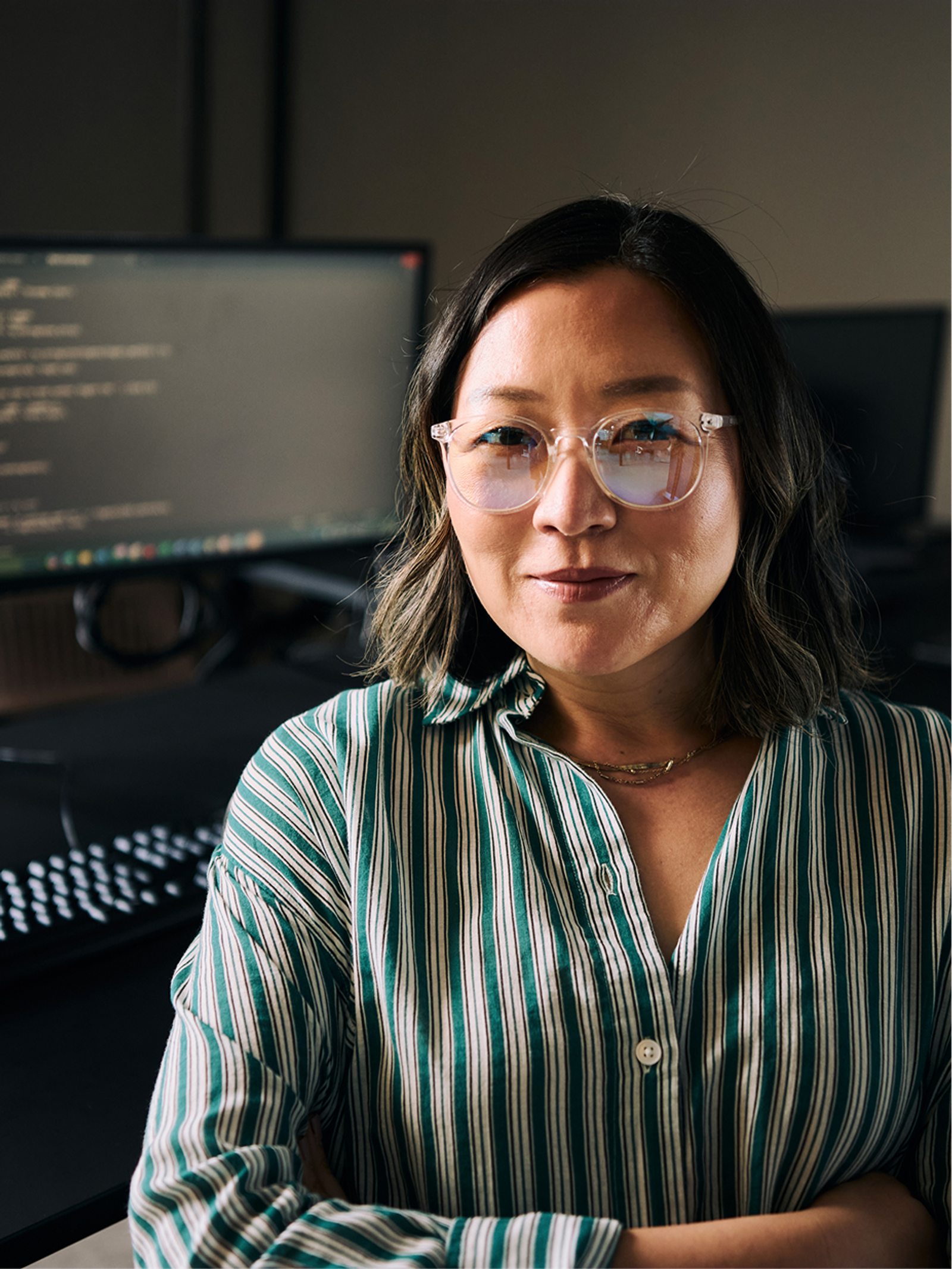 An engineer standing with arms crossed at a desk with code on screen