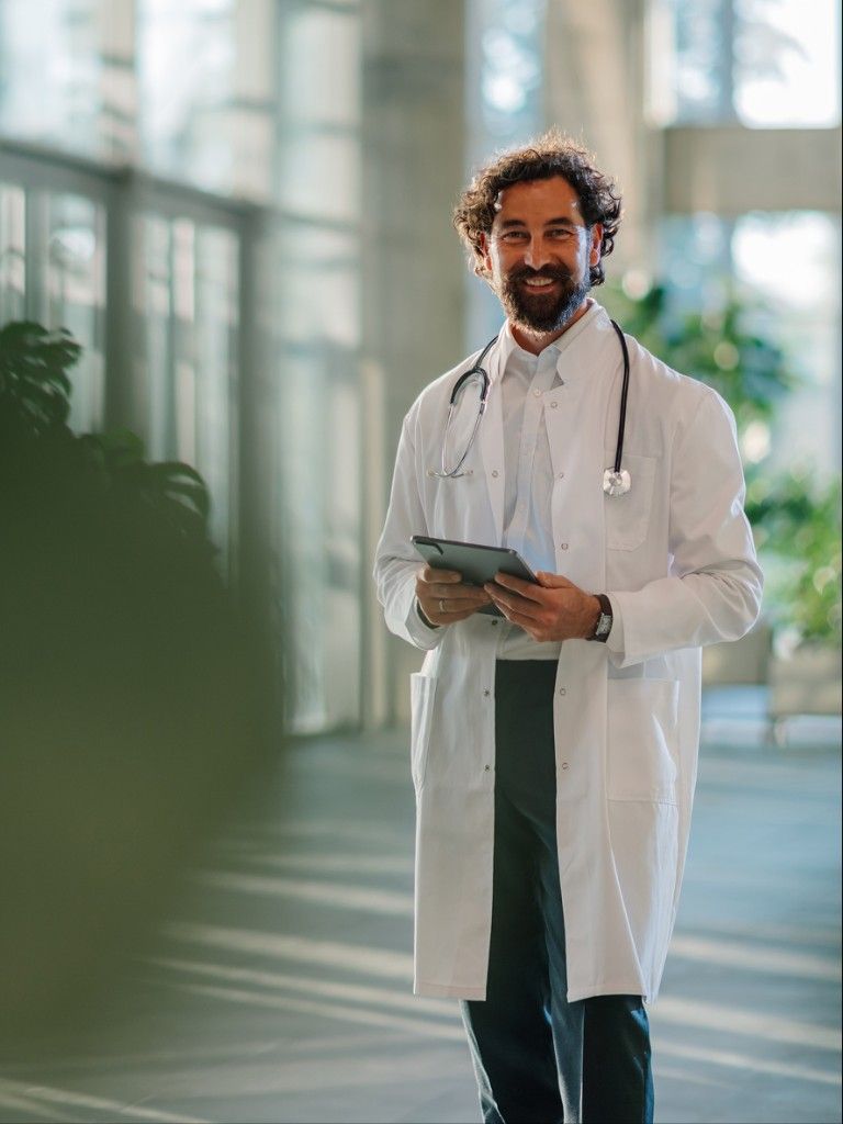A smiling physician holding a tablet in a hospital corridor