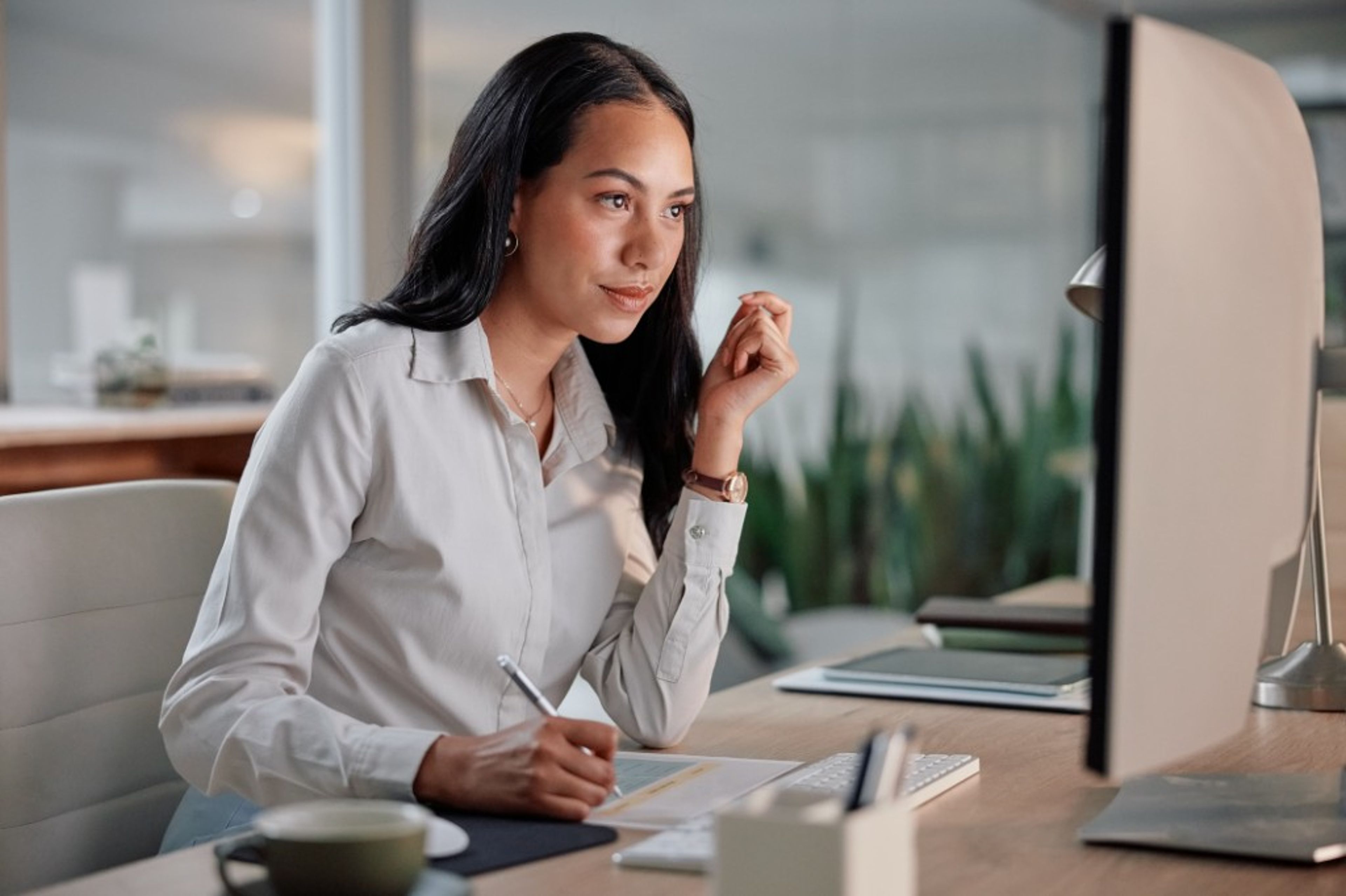 A professional working at a desk, reviewing documents on a computer screen in a bright office.