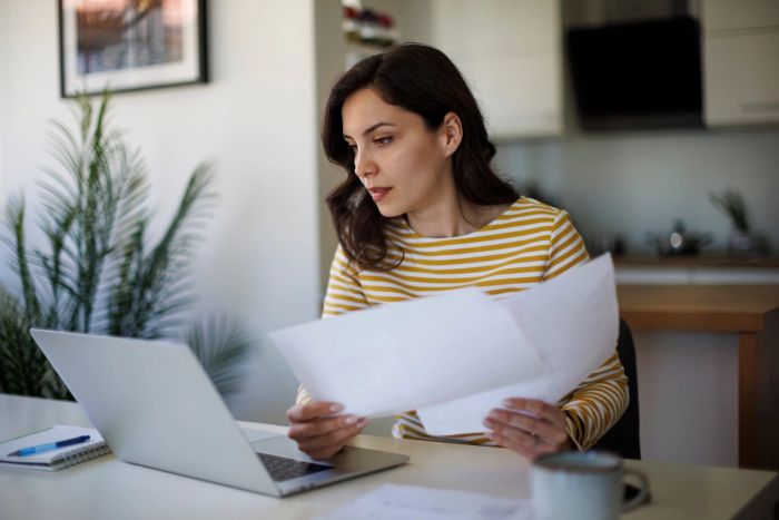 A young woman sits at her desk and looks intently at papers containing a USCIS Request for Evidence.