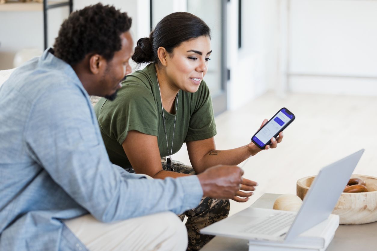 A married couple look over documents together on their laptop and mobile device.