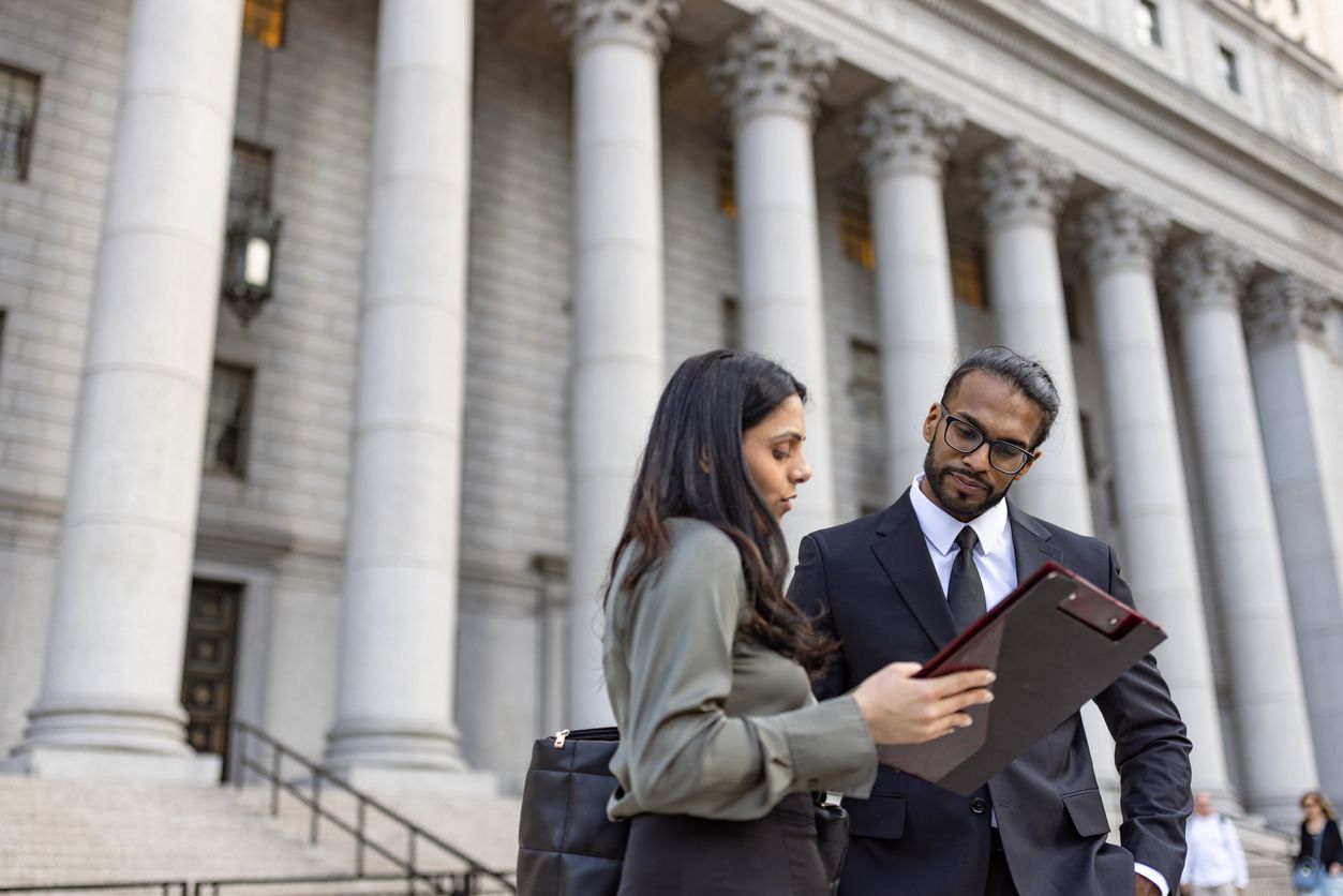 An attorney and their client standing in front of the exterior of a courthouse.