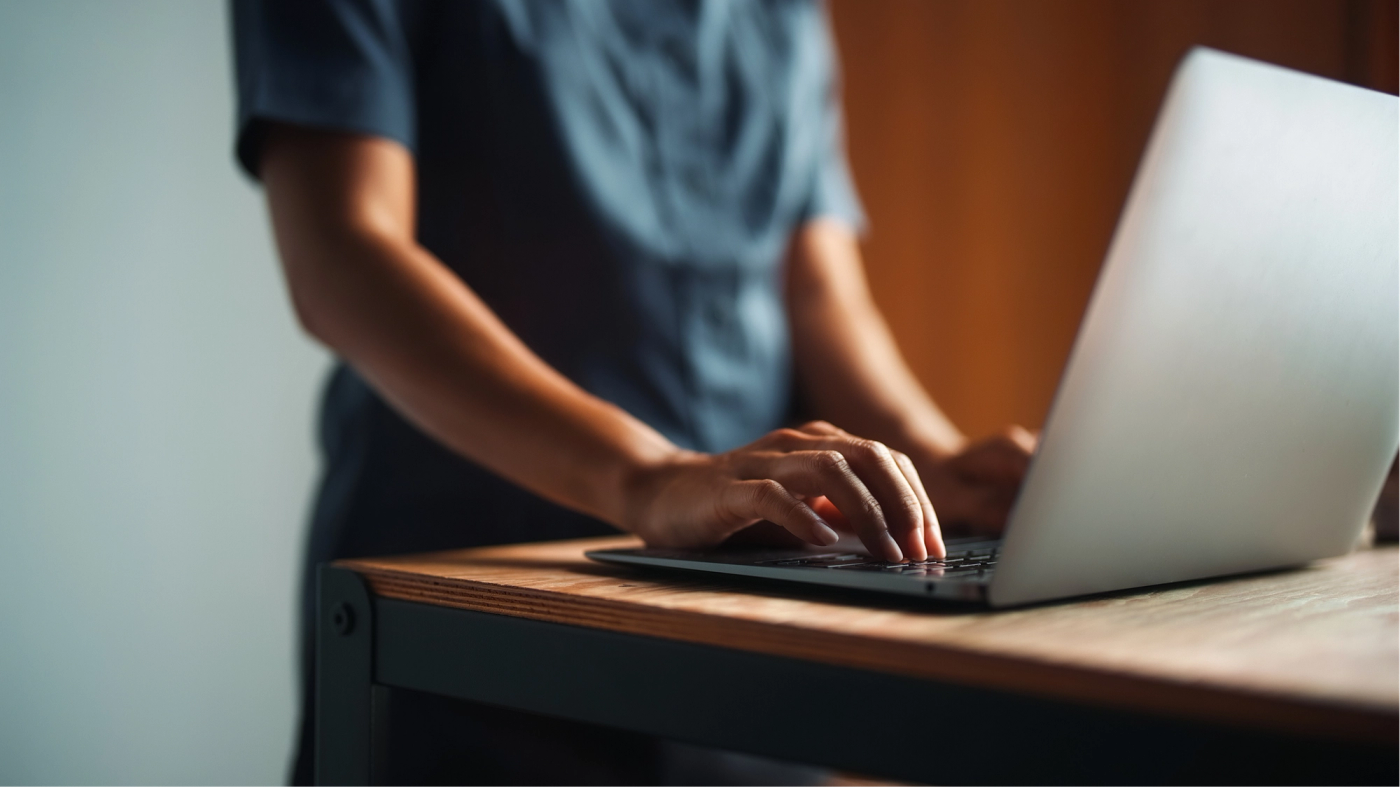 Close-up of hands typing on a laptop at a wooden desk