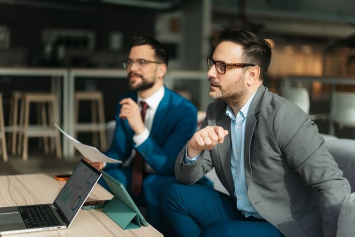 Two businessmen investors are discussing an investing strategy while looking at a laptop and documents.