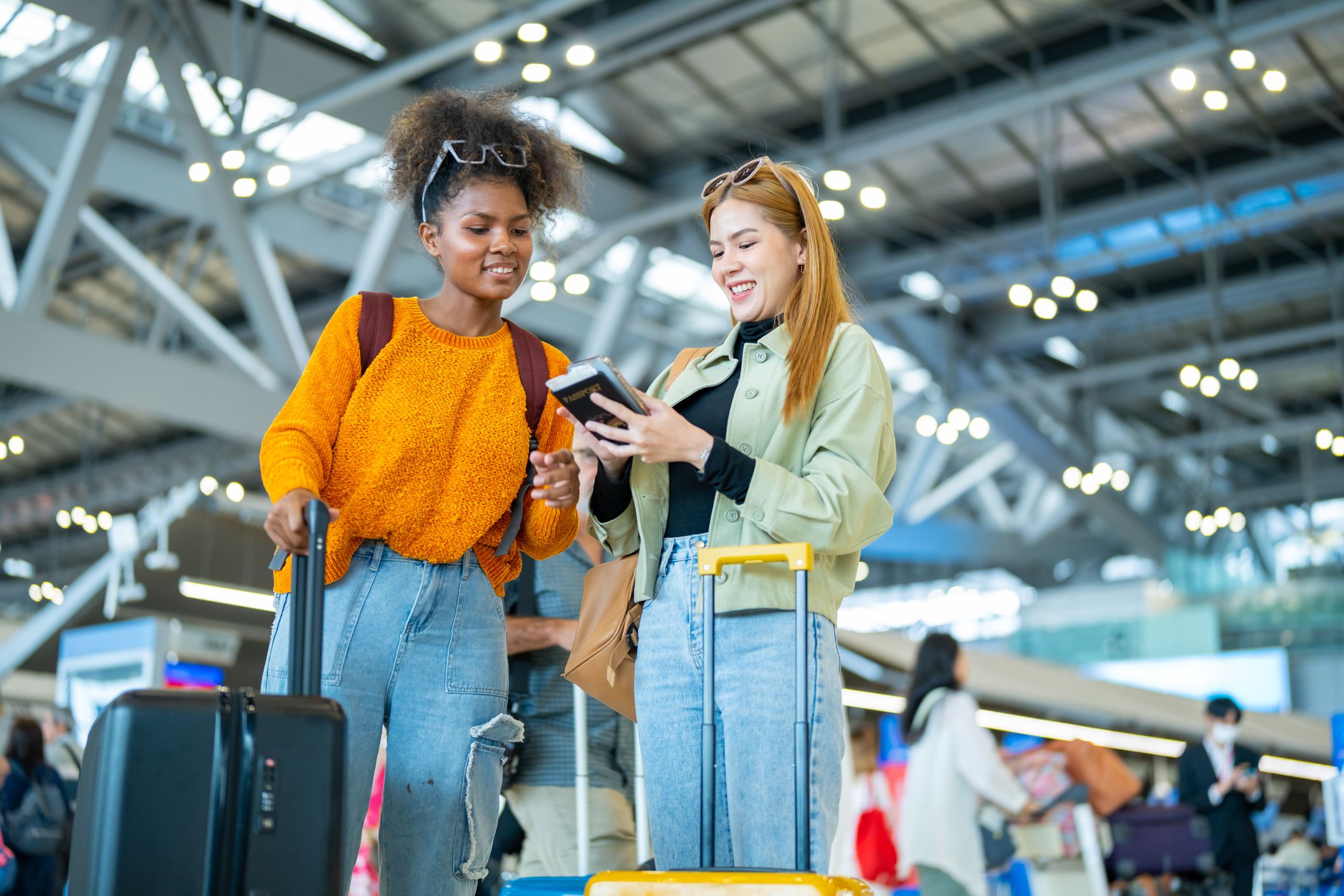 Two women friends with luggage walk together through an airport terminal after expedited B-1/B-2 visa interviews